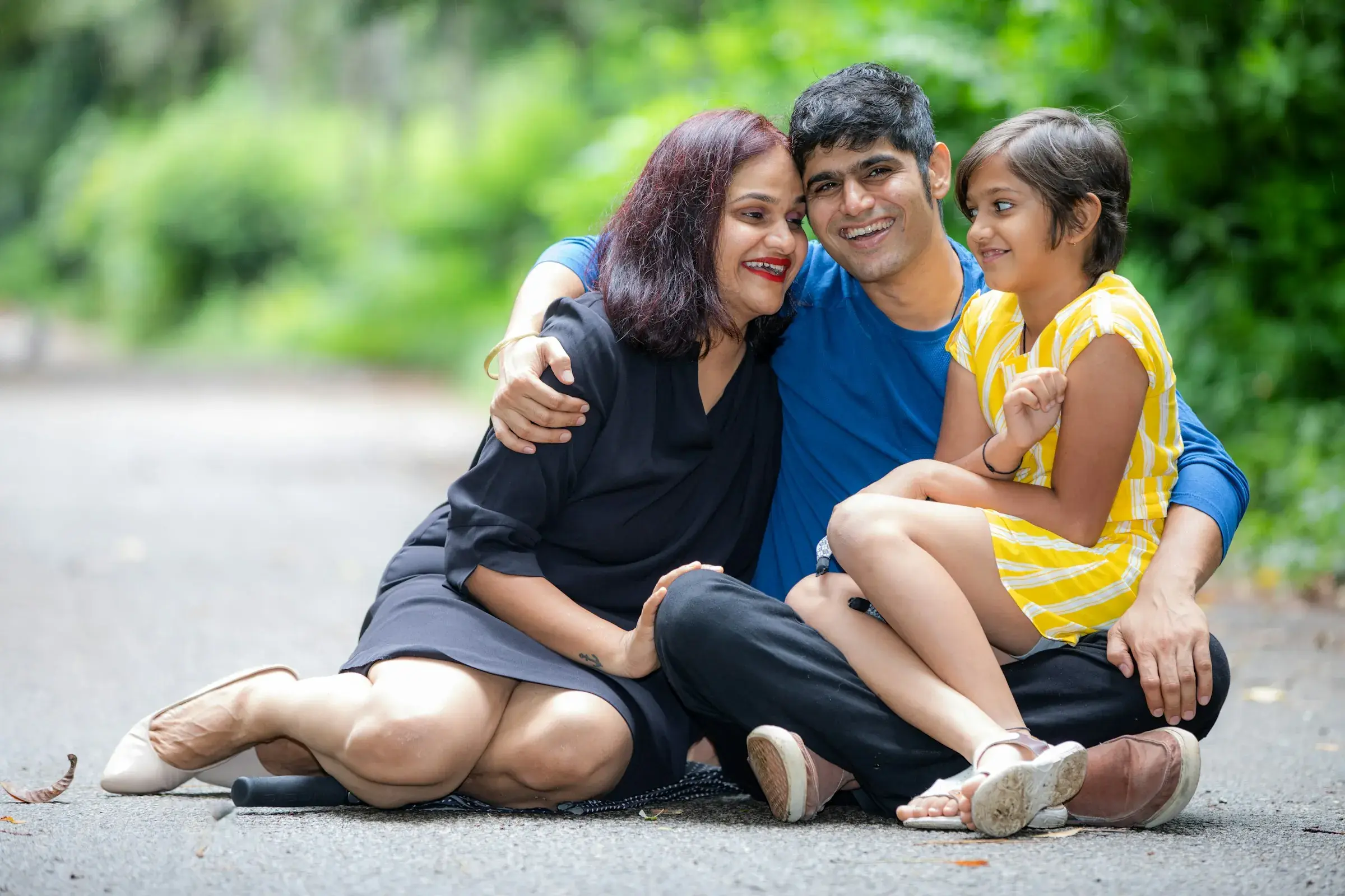 A mother, father and daughter sitting close together outdoors, laughing